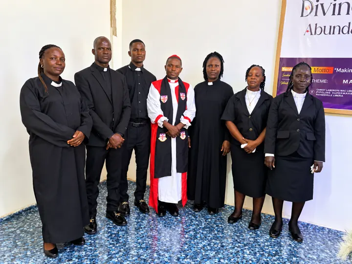 The Bishop in red and white vestments standing with newly ordained clergy